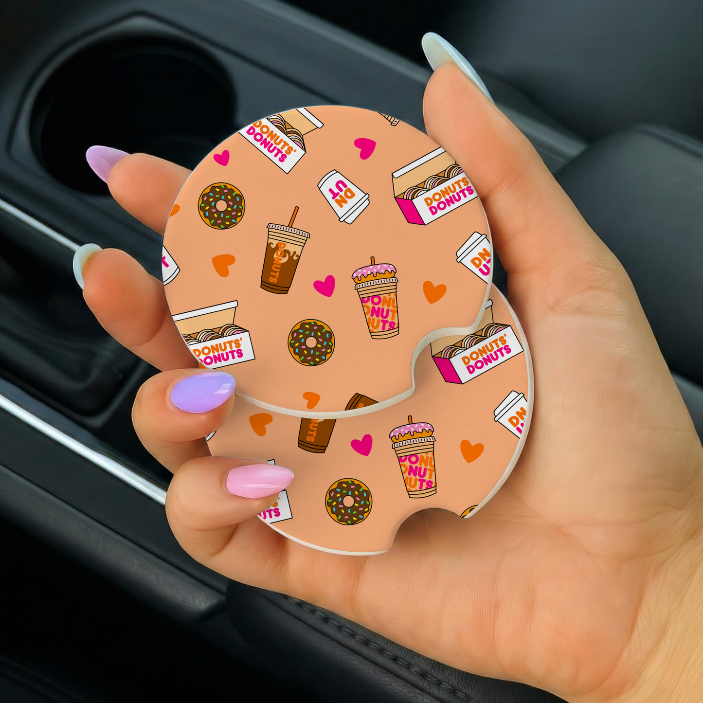 Car coaster with donut and coffee design held by a hand in a car.