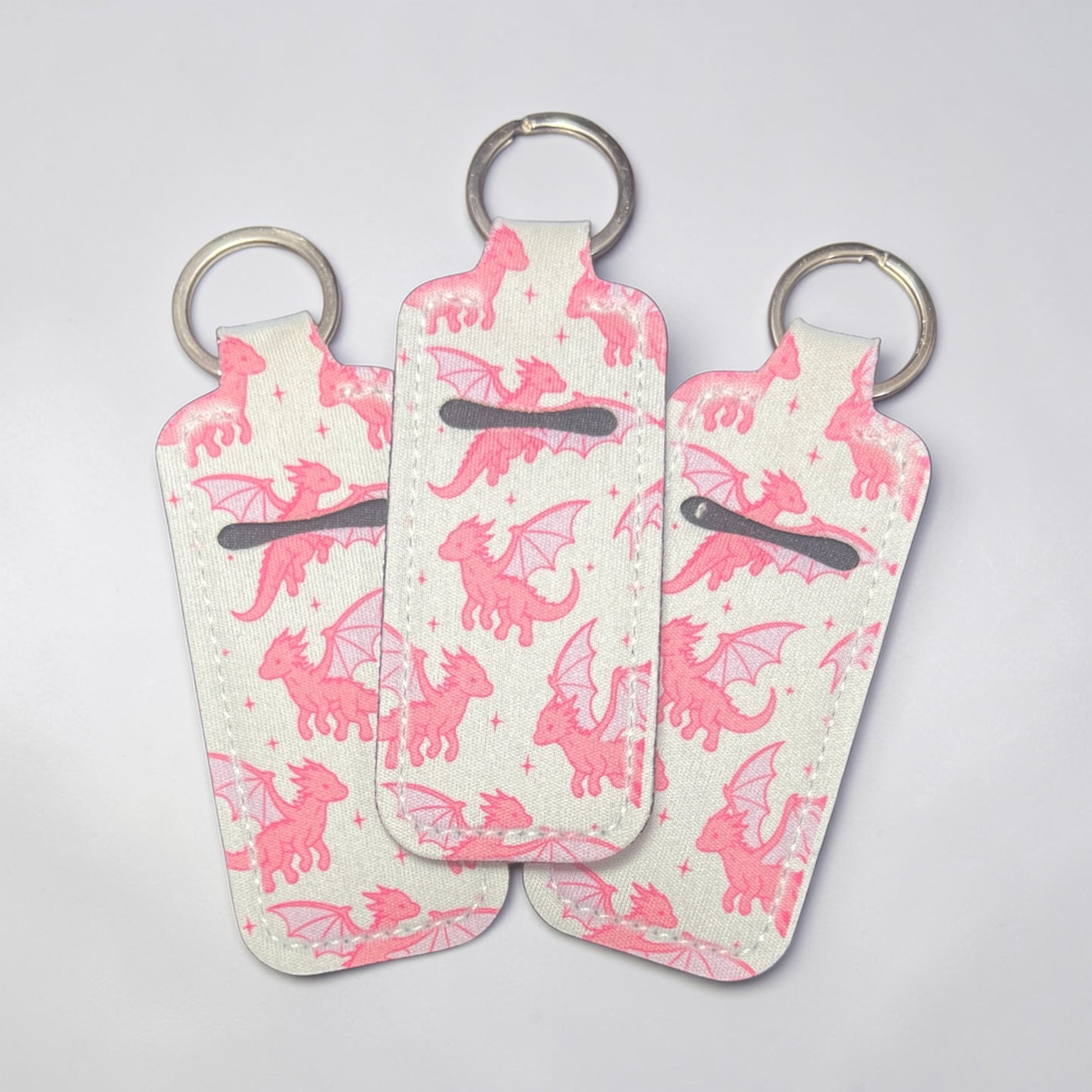 Three keychains with pink dragon patterns on a light gray background