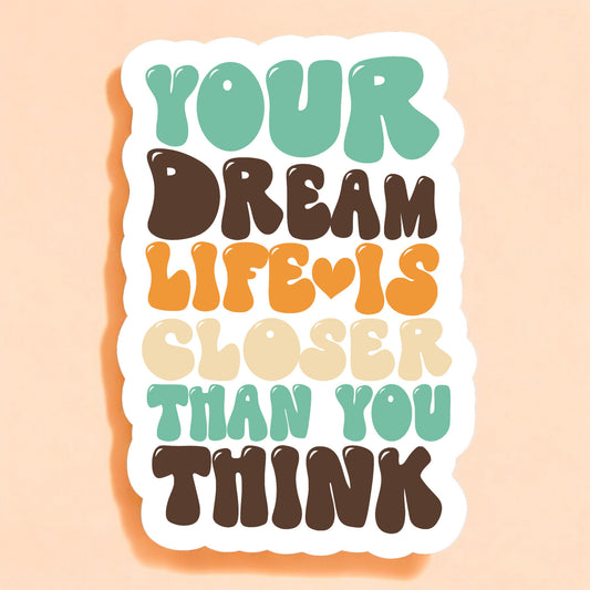 a white sticker that reads your dream life is closer than you think in bubble letters in teal blue green, brown, and mustard yellow