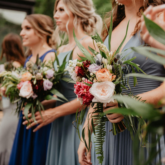 Three women in formal attire holding floral bouquets outdoors.