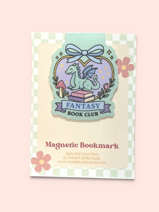 A decorative magnetic bookmark card for a fantasy book club, featuring a whimsical dragon illustration, flowers, and the text 'Magnetic Bookmark' and 'Made with Good Vibes by Midnight Dahlia Studio' on a pale pink background.