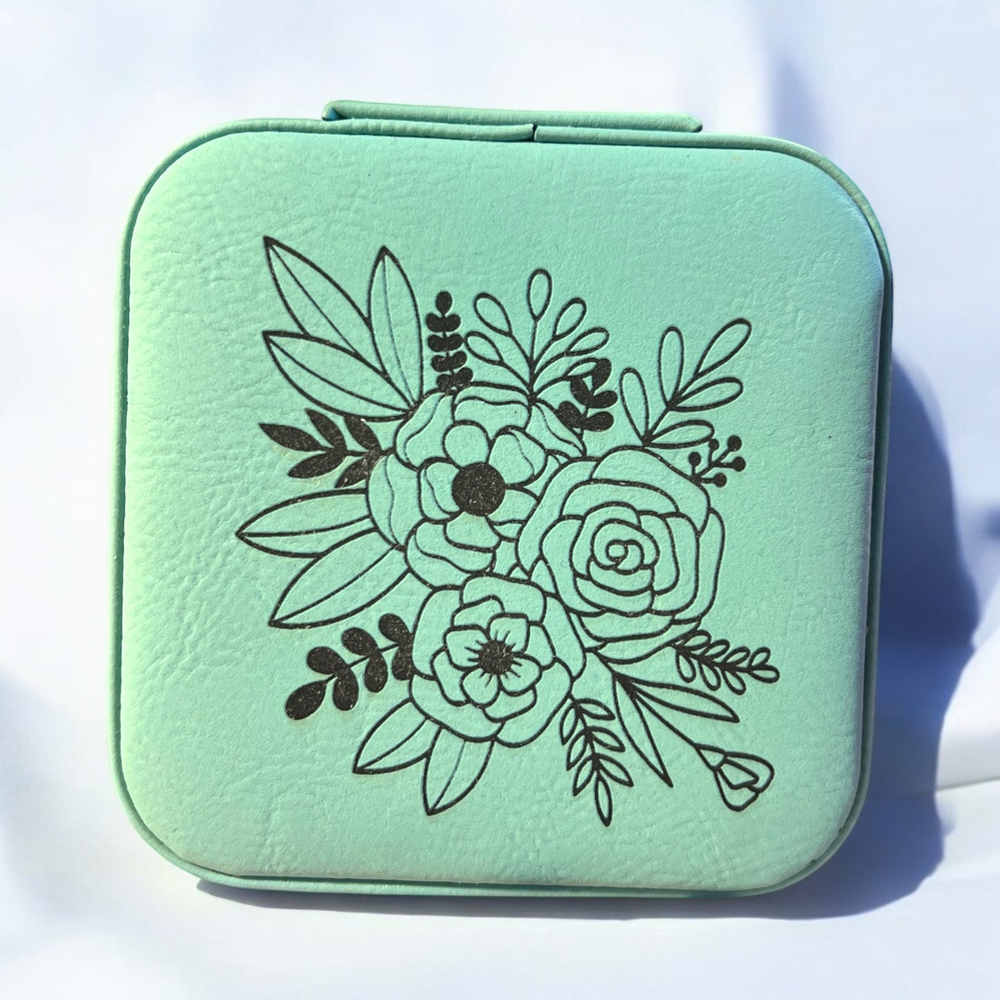 a teal jewelry box engraved with black floral pattern