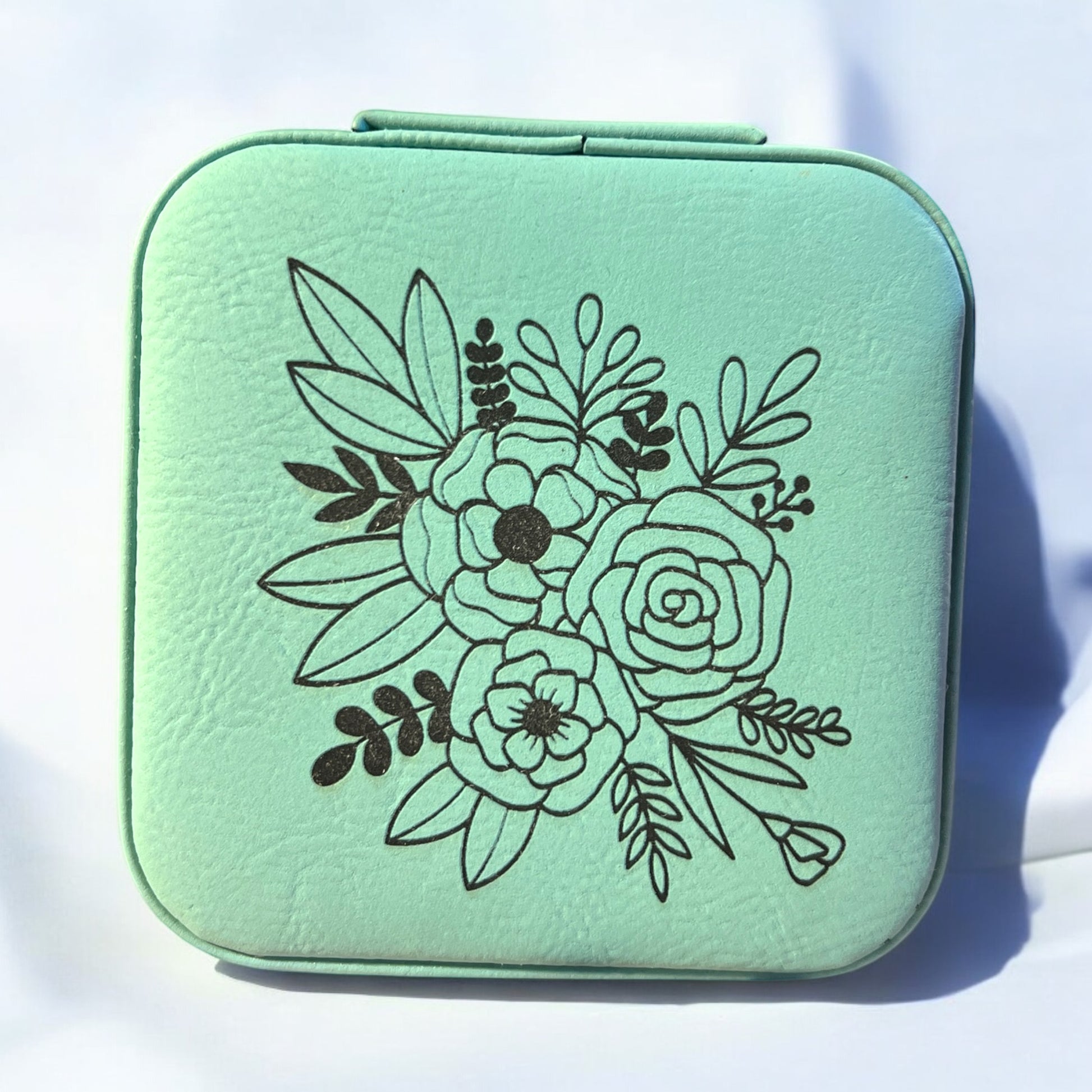 a teal jewelry box engraved with black floral pattern