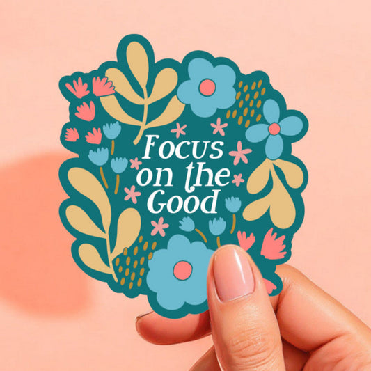 a sticker with a blue-green background that reads focus on the good in white surrounded by colorful flowers