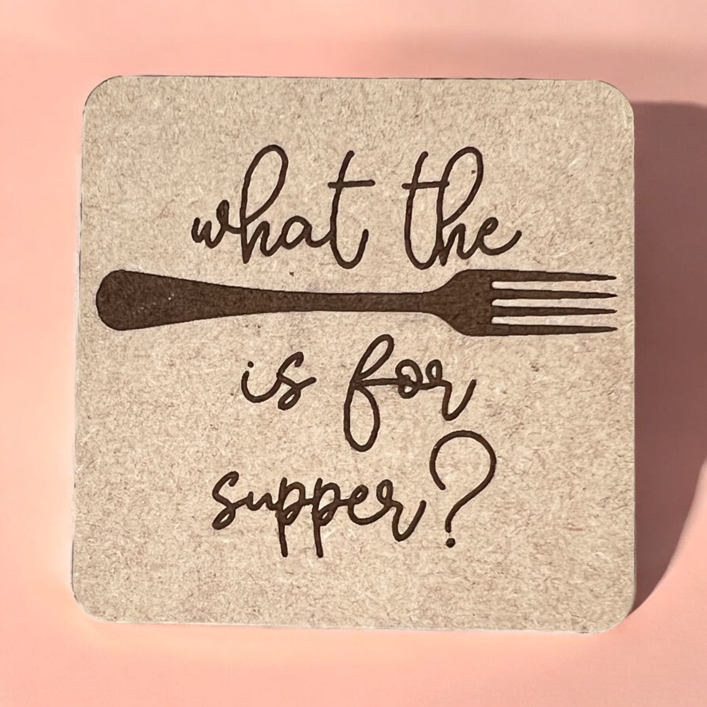 A square magnet with a humorous quote printed on it, placed against a pink background.