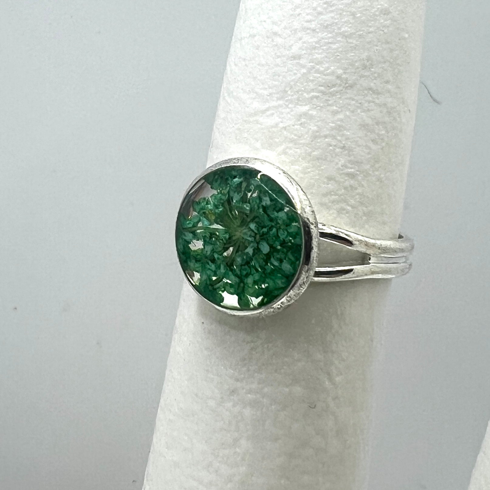 Silver ring with a green queen anne's lace flower on a white cylindrical stand.