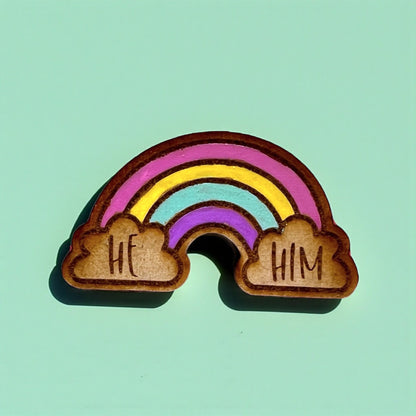 Wooden rainbow charm with 'HE' and 'HIM' on a light green background