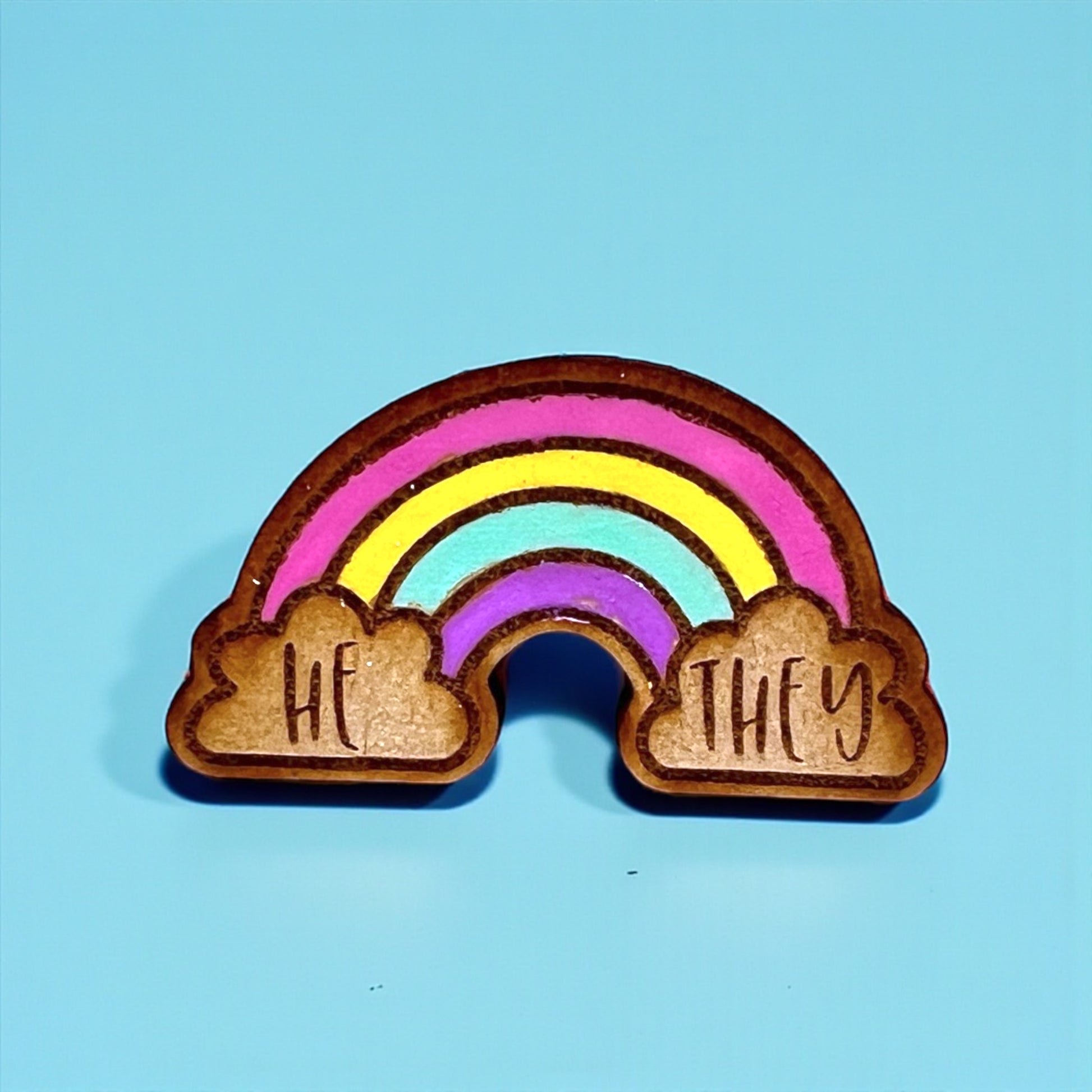 Rainbow-shaped object with 'HE' and 'THEY' engraved on a blue background