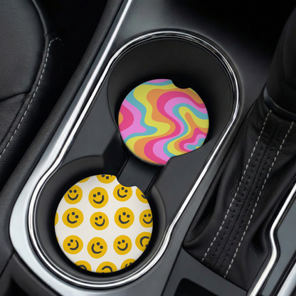 Two car cup holders with colorful and smiley-patterned coasters in a vehicle interior.