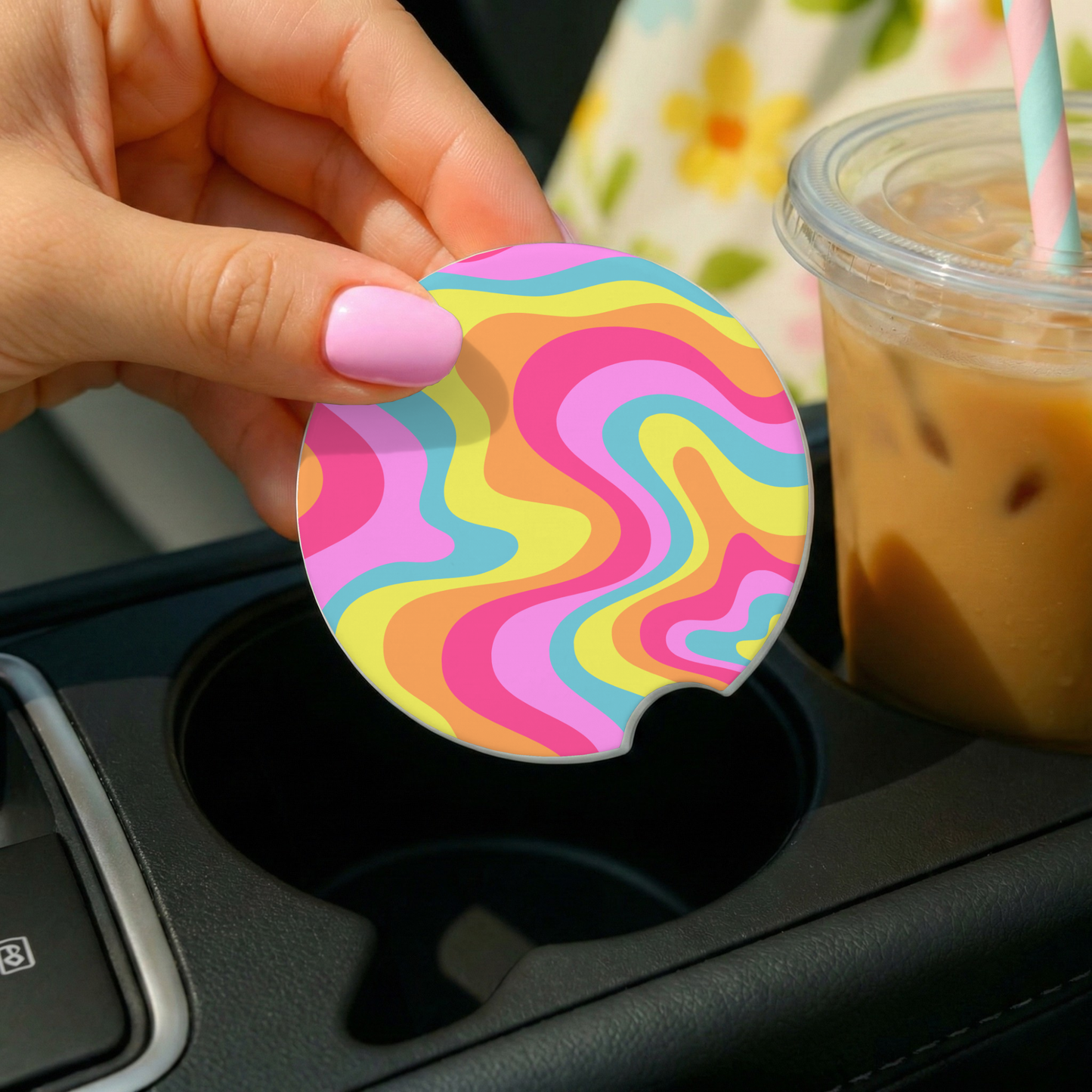 Colorful swirl-patterned car coaster held by a hand over a car cup holder with a drink in the background.