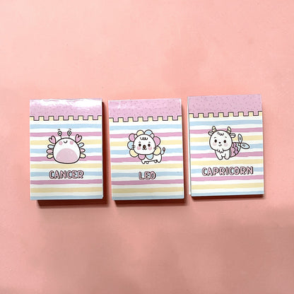 Three small bookmarks with zodiac designs and names on a pink background