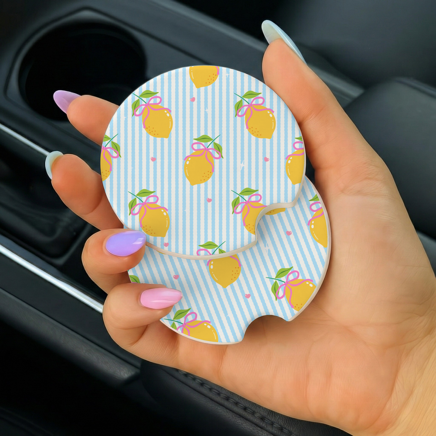 a hand holding two lemon-themed car coasters