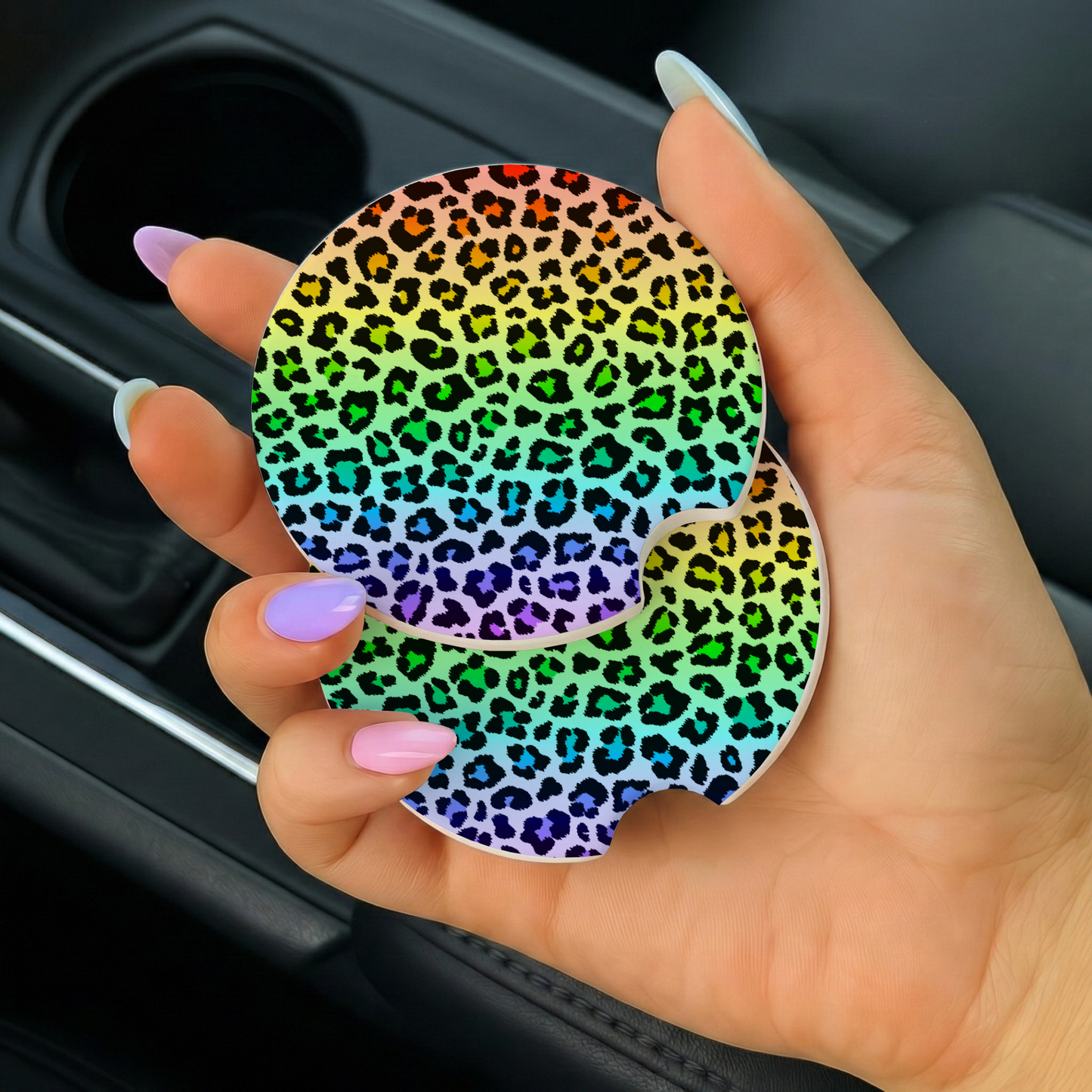Hand holding a rainbow leopard print car coaster in a vehicle.