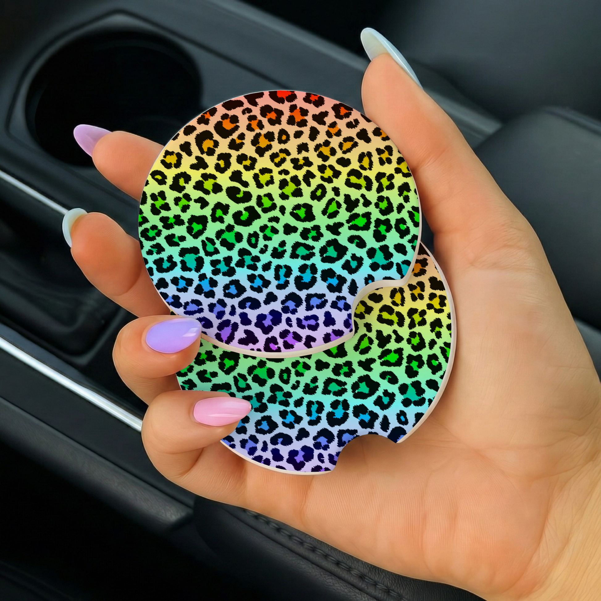 Hand holding a rainbow leopard print car coaster in a vehicle.