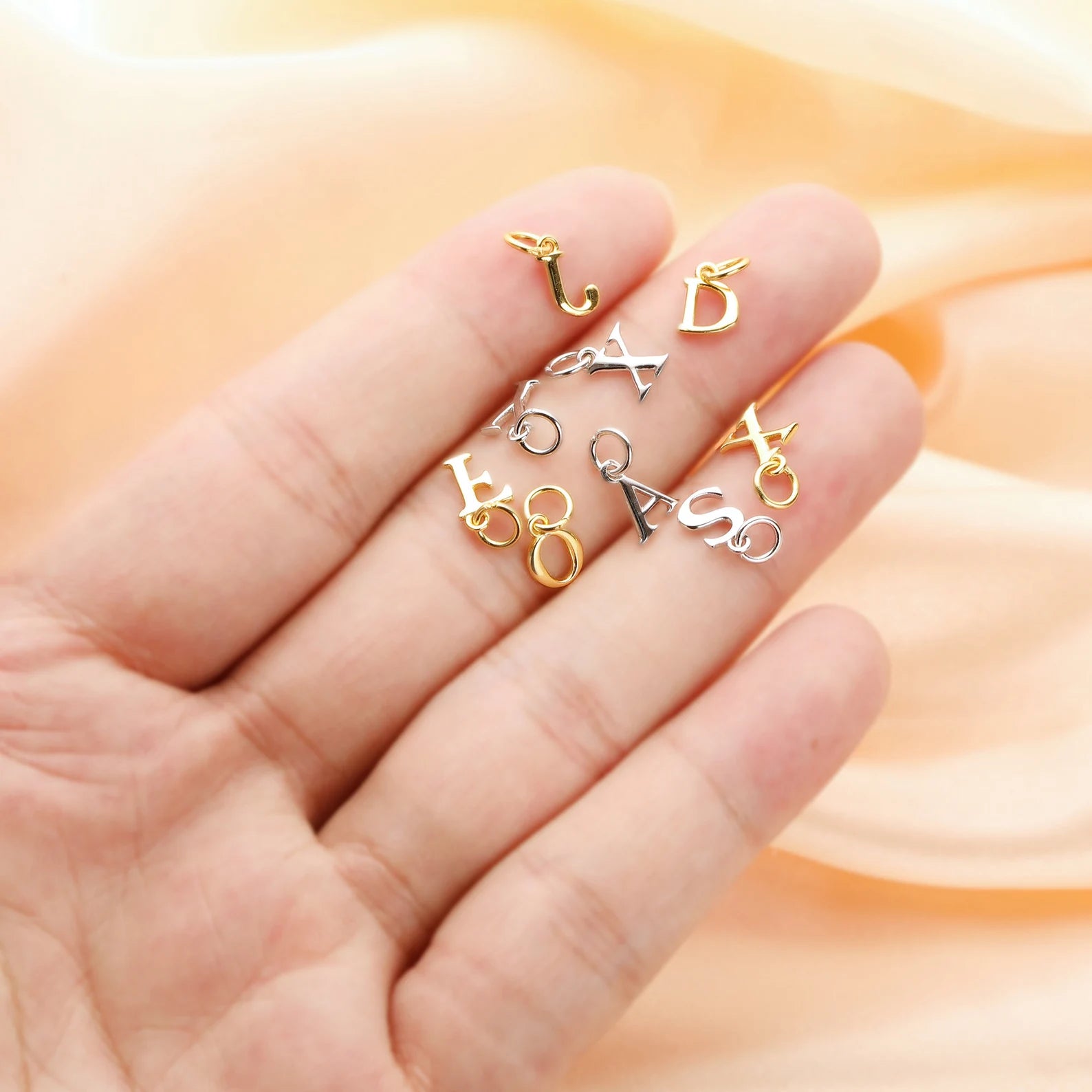 Gold, silver, and bronze letter charms on a hand with a soft peach background
