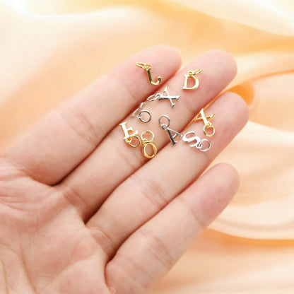 Gold, silver, and bronze letter charms on a hand with a soft peach background