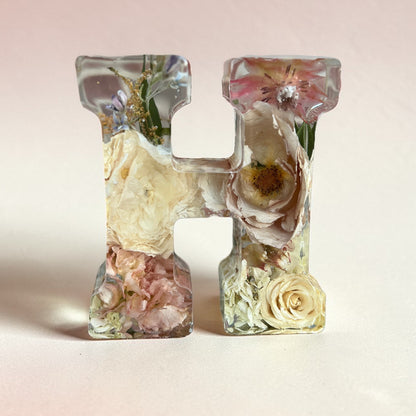 Clear resin letter 'H' with embedded flowers on a light pink background