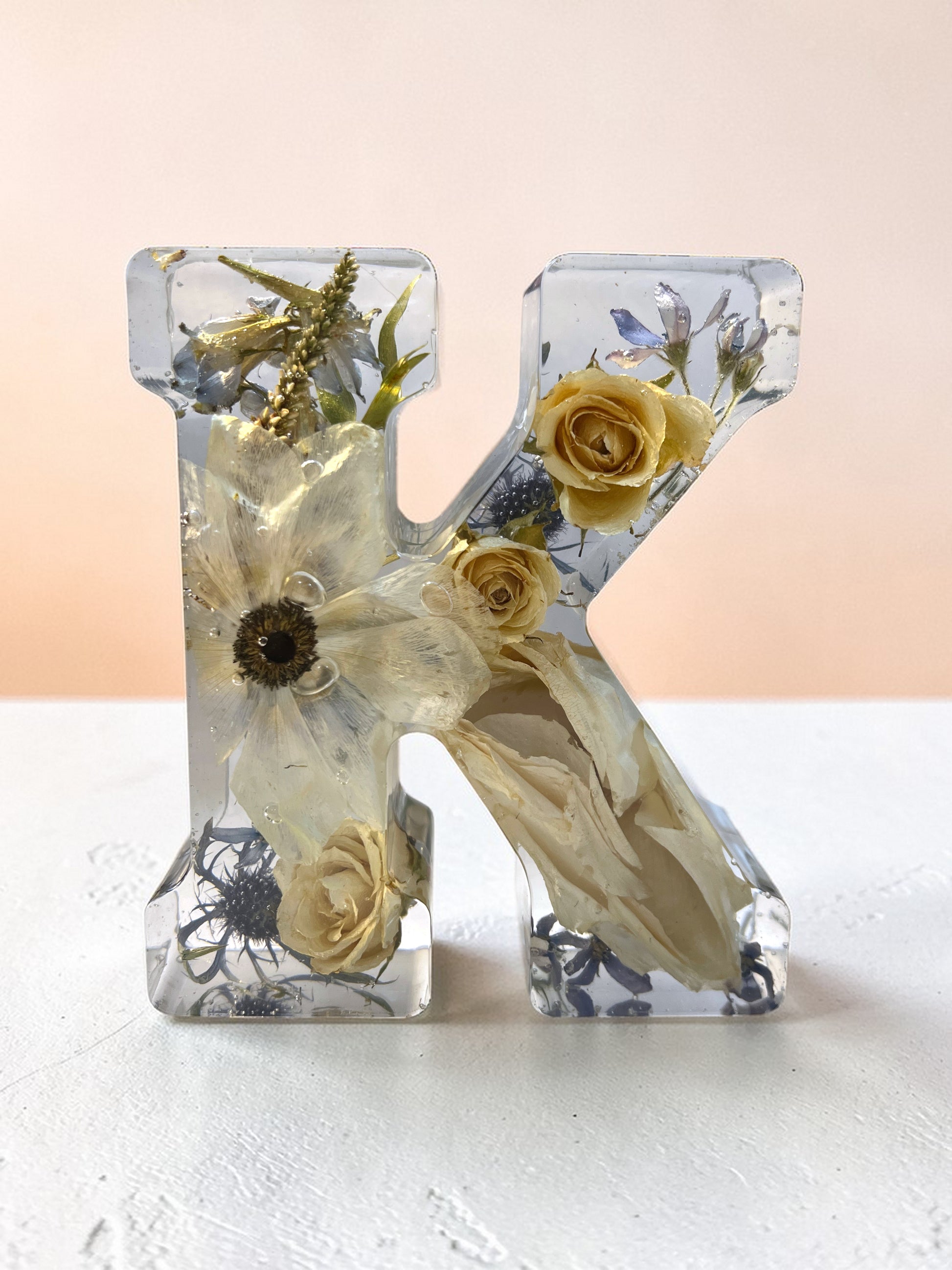 Clear resin letter 'K' with pressed flowers on a white background