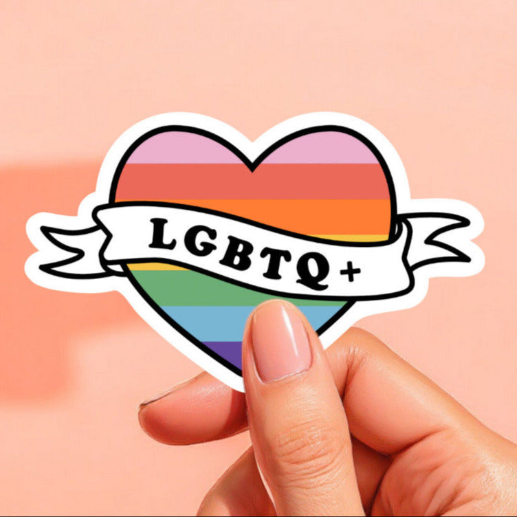 a heart shaped sticker printed with a rainbow with a banner that reads lgbtq+