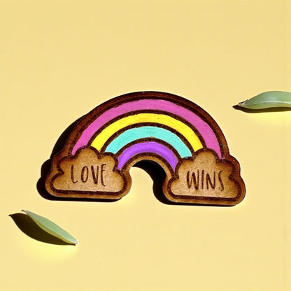 Wooden rainbow-shaped pin with 'Love Wins' on a yellow background