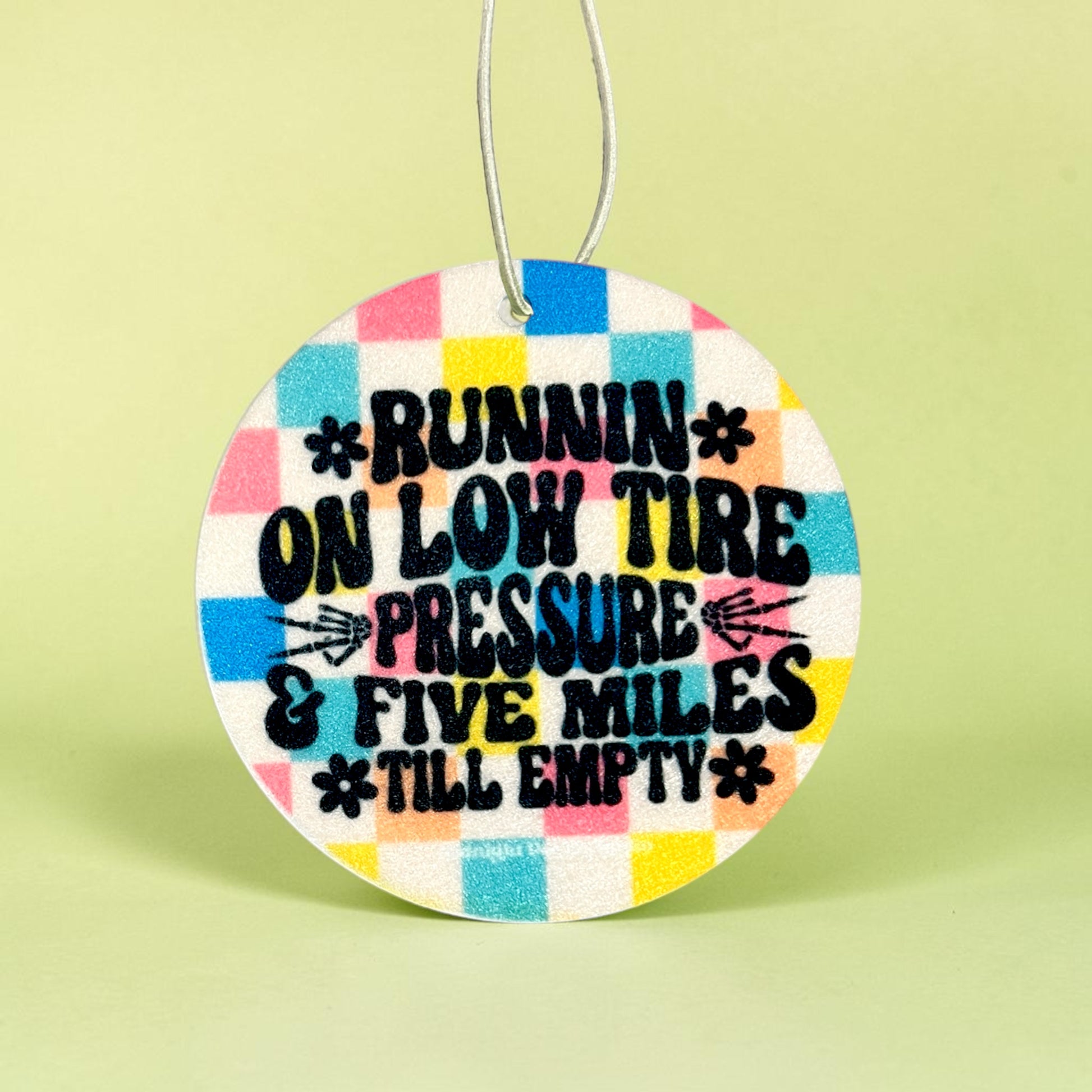 Round colorful car air freshener with humorous text on a light green background