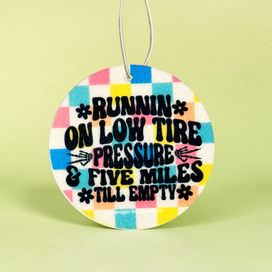 Round colorful car air freshener with humorous text on a light green background