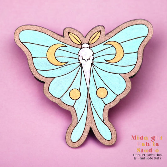 a wooden luna moth magnet hand painted in teal, yellow, and white