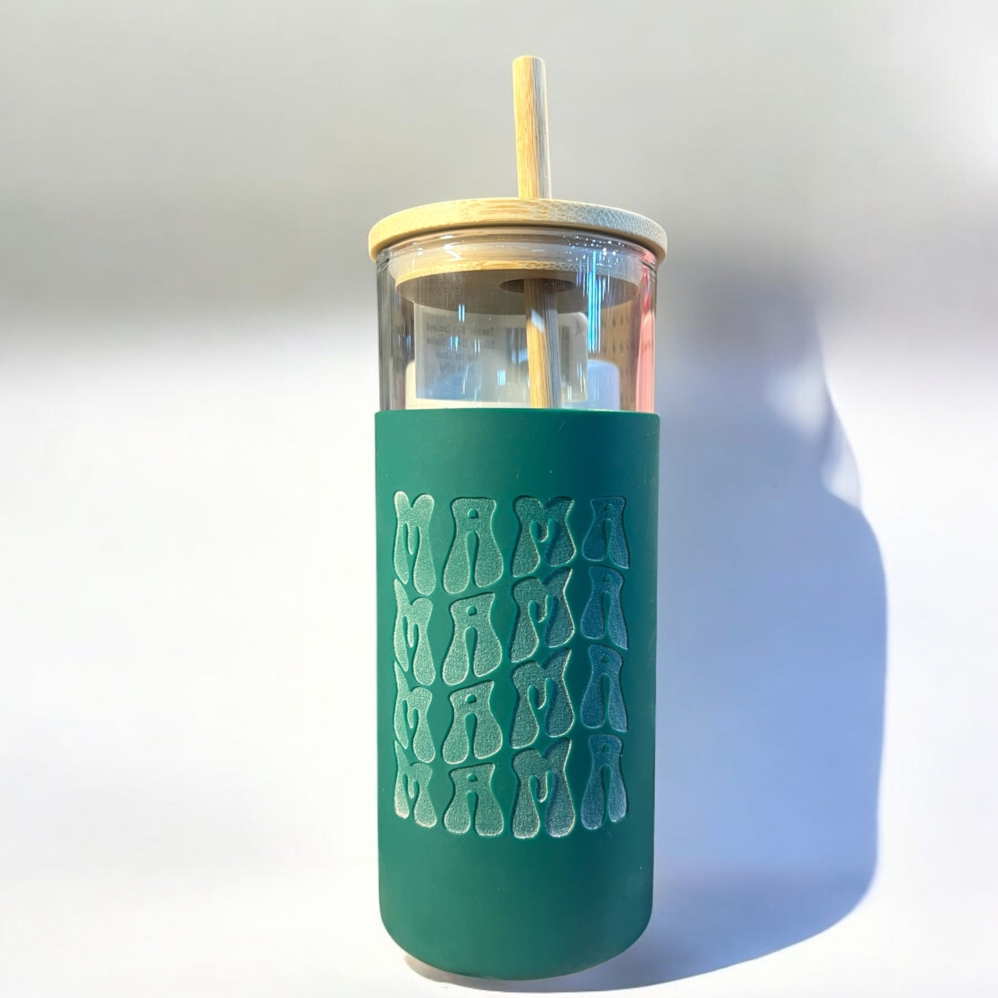 A green tumbler with a clear glass body, a silicone engraved a bamboo straw, and the text 'mama'