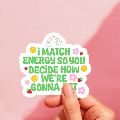 A colorful sticker with the text 'I MATCH ENERGY SO YOU DECIDE HOW WE'RE GONNA ACT' printed on it, featuring various playful icons like smiley faces and strawberries.