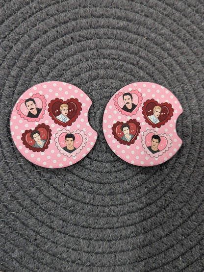 Two pink coasters with heart designs on a gray textured surface