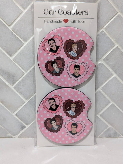 Two pink car coasters with heart designs on a white card against a tiled wall background.