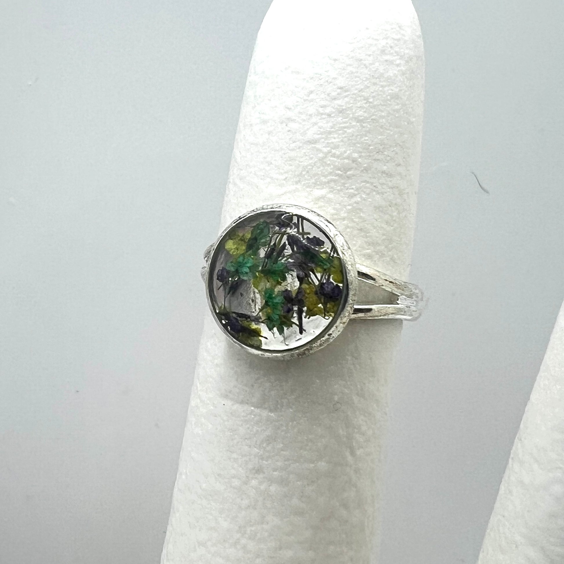 Silver ring with a circular design on a white stand against a gray background