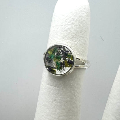 Silver ring with a circular design on a white stand against a gray background