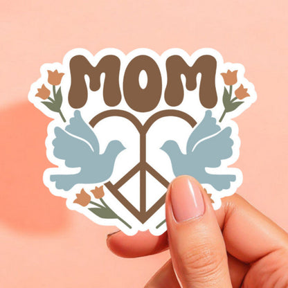a sticker with the word mom with a heart shaped peace sign with a light blue dove on either side