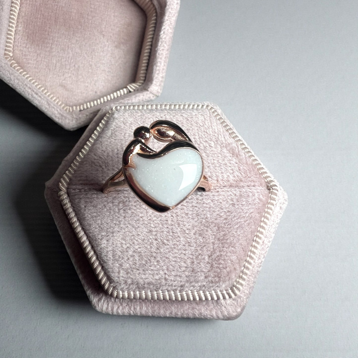 Heart-shaped ring with light blue stone in a pink jewelry box on a gray background