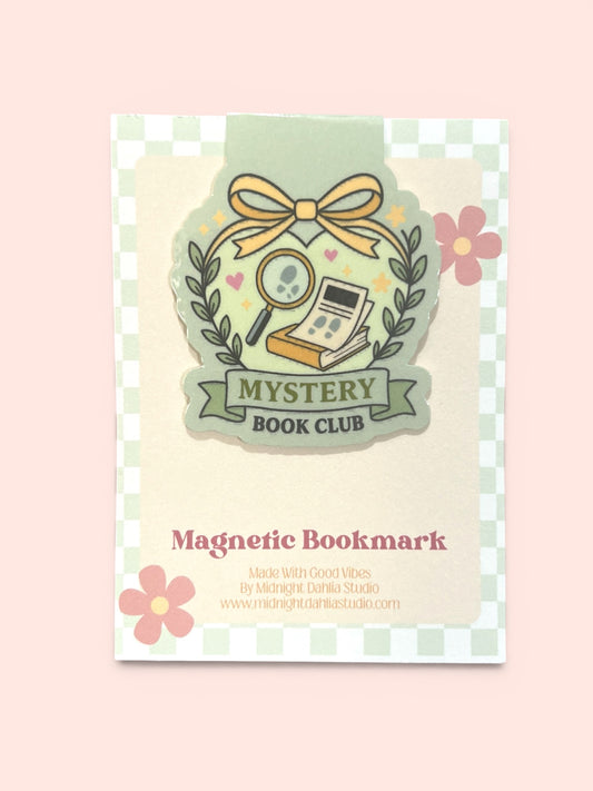 A decorative product card for a 'Mystery Book Club' magnetic bookmark, featuring a pastel illustration of a book, magnifying glass, and bow, with pink flowers and a green-and-white checkered border on a pale pink background.
