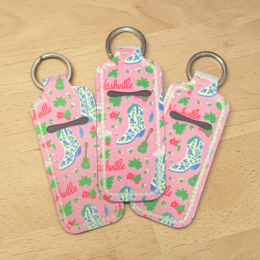 Three pink keychains with floral patterns and 'Nashville' text on a wooden surface