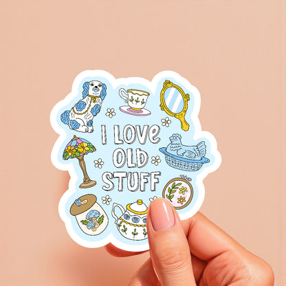 Sticker with vintage-themed illustrations and 'I love old stuff' text held by a hand on a beige background