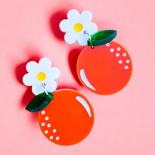 A pair of dangle earrings made of acrylic with the bottom in a round shape with white accents to look like an orange fruit, hanging from a white daisy post with a yellow center and a leaf.  perfect summer accessory for women woman.