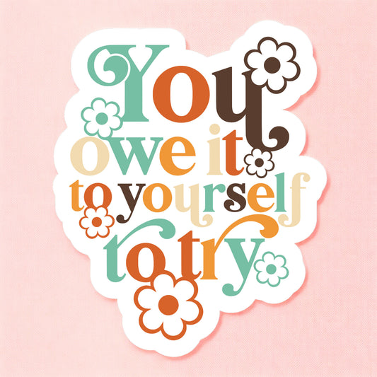 a white sticker that reads you owe it to yourself to try in colorful retro lettering surrounded by daisies in matching colors