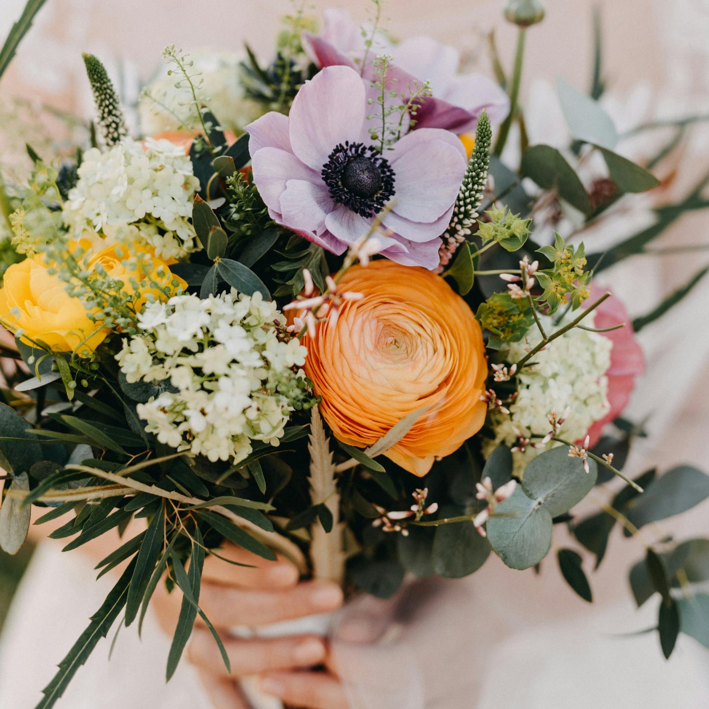 Bouquet of flowers with orange, purple, and green colors held by a person.