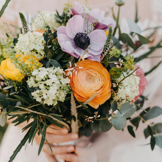 Bouquet of flowers with orange, purple, and green colors held by a person.