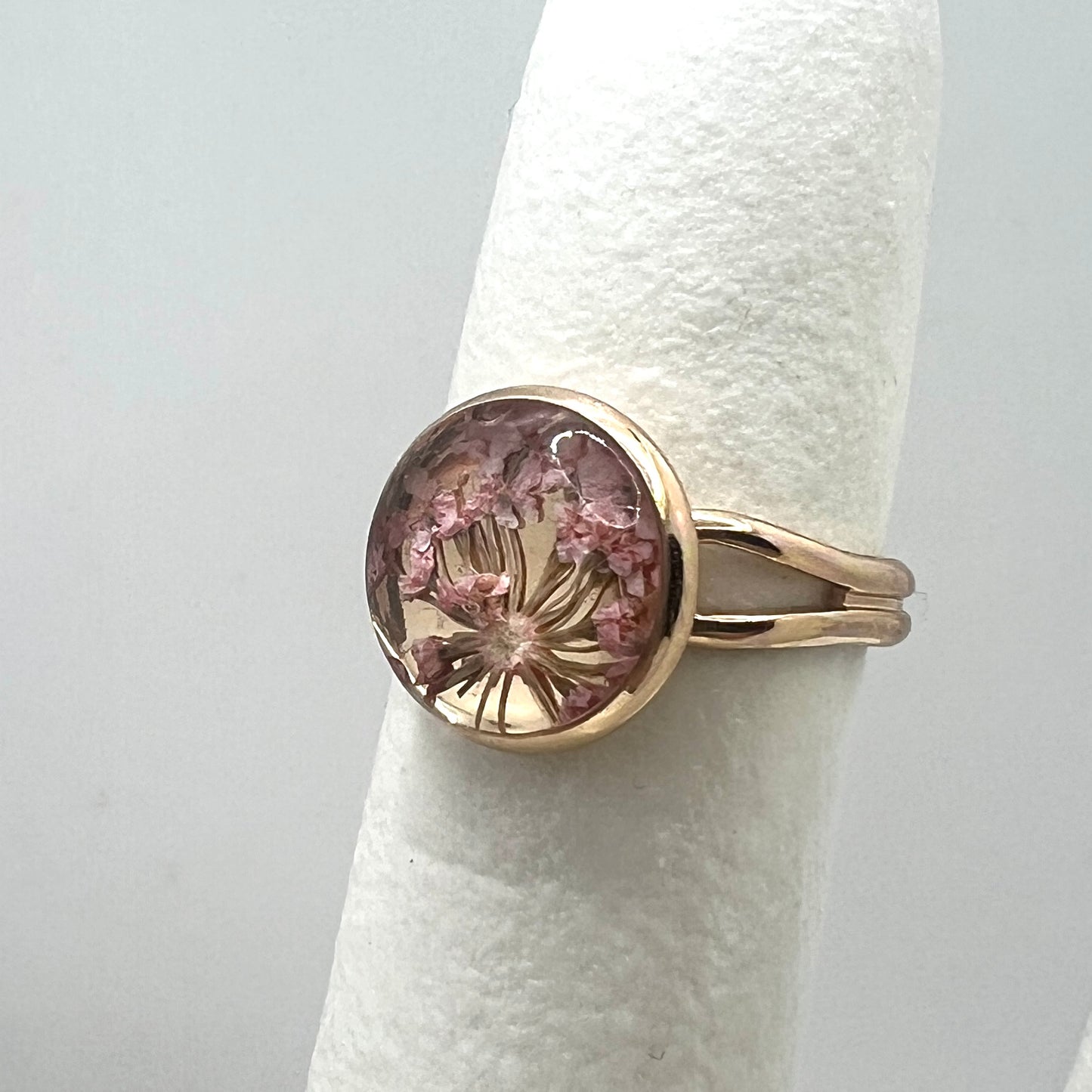 Gold ring with a pink queen anne's lace real pressed flower on a white background