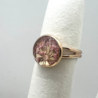 Gold ring with a pink queen anne's lace real pressed flower on a white background