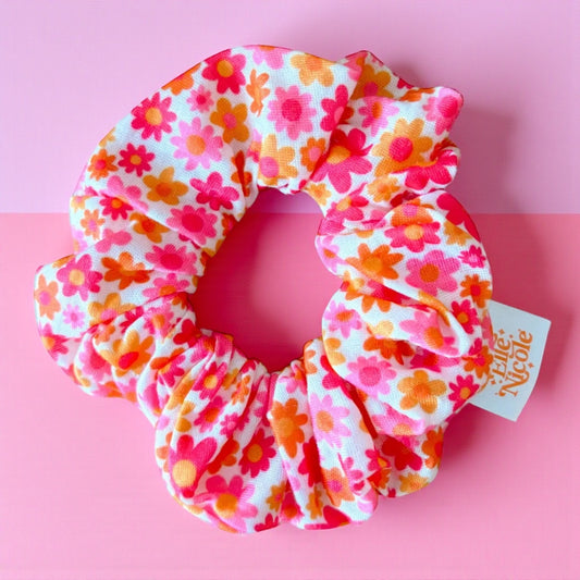 Floral patterned scrunchie with a visible brand tag on a pink background