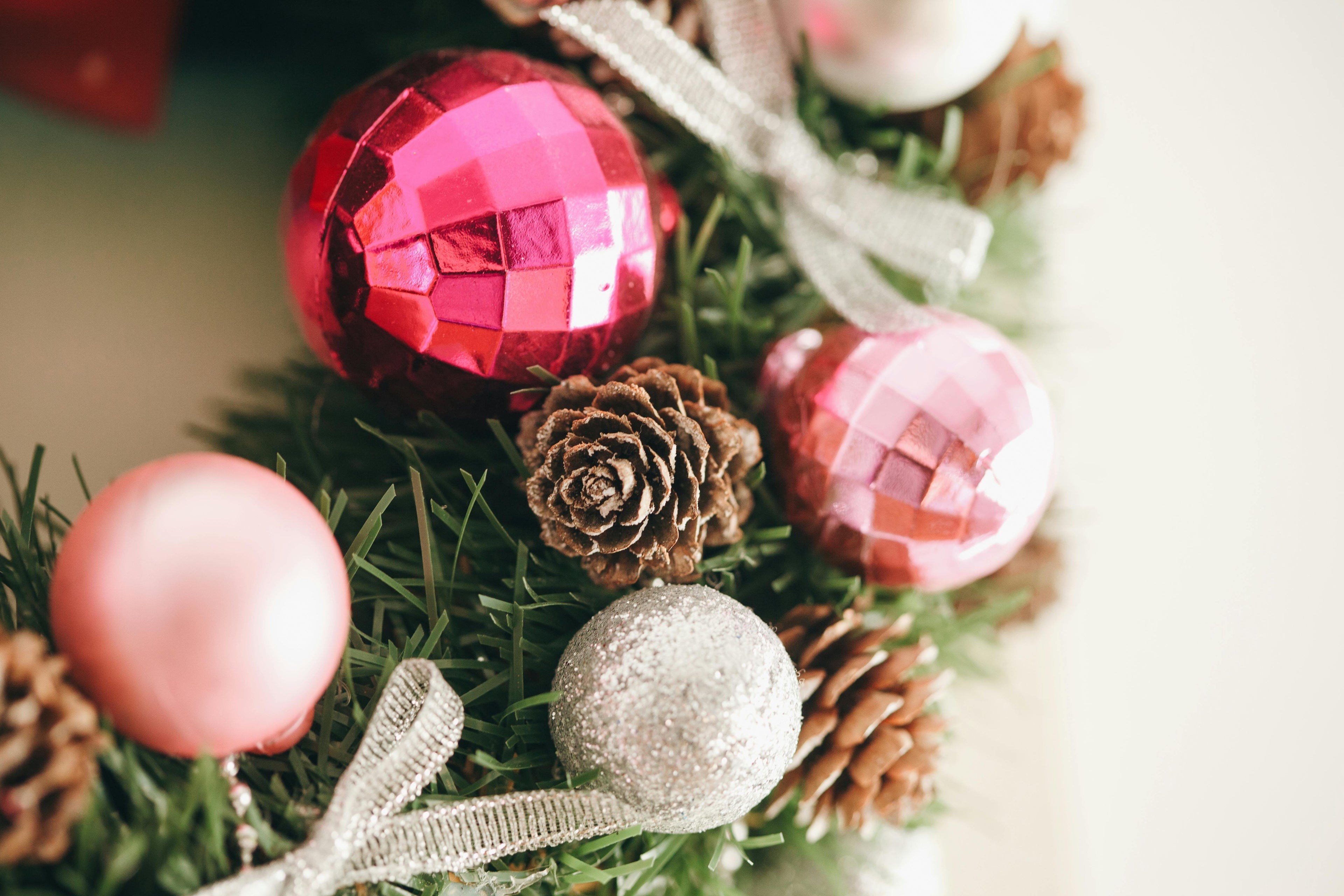Close-up of Christmas ornaments on a green wreath with red, pink, and silver balls.