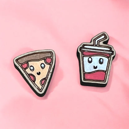 Two cute earrings, one shaped like a pizza slice and the other like a drink with a straw, on a pink background.