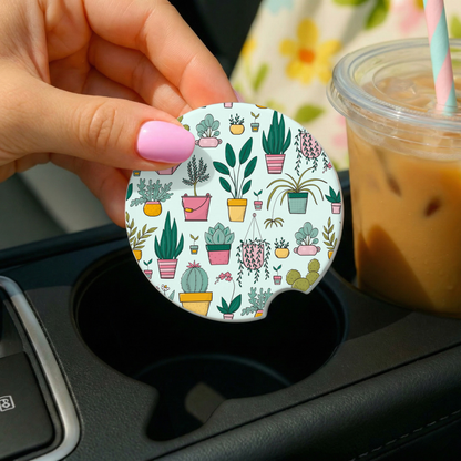 Hand holding a car coaster with plant pattern next to a drink in a car cup holder.