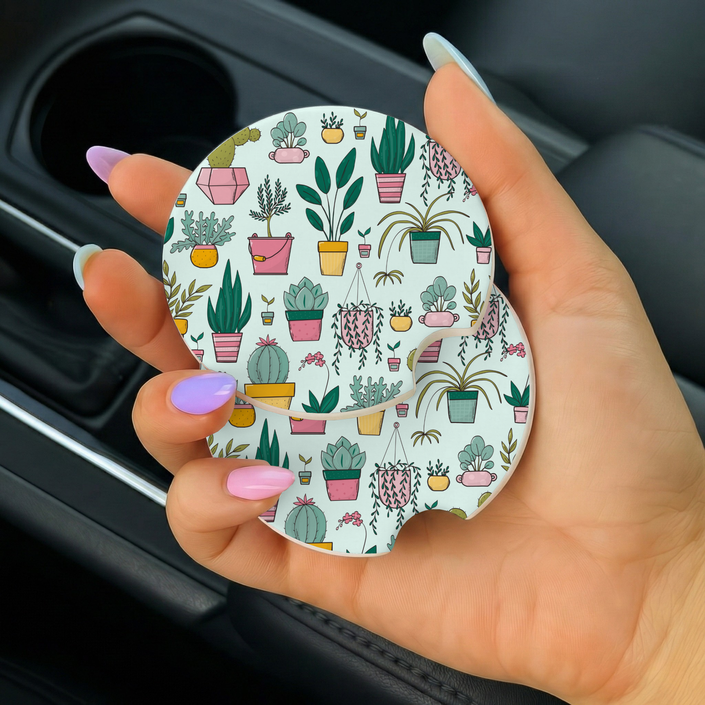 Hand holding a round car coaster with plant pattern inside a vehicle.