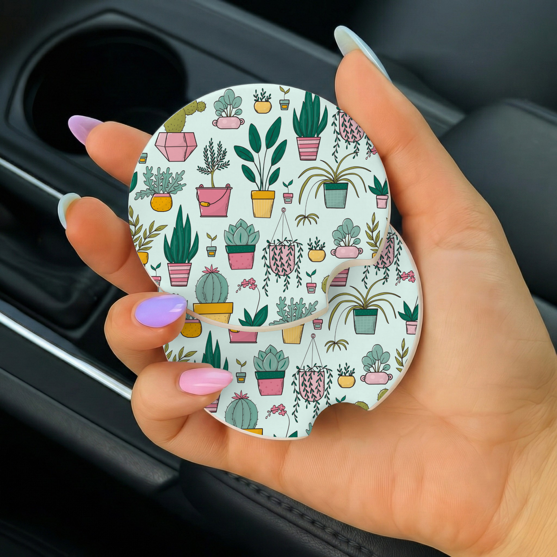 Hand holding a round car coaster with plant pattern inside a vehicle.